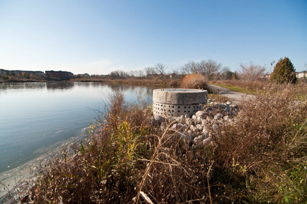 A perforated concrete pipe forms part of a stormwater management system in a suburban pond.

